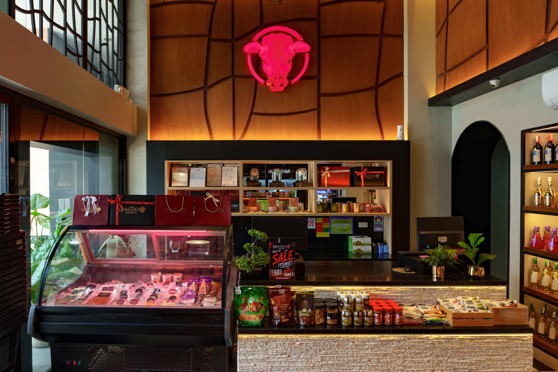 Inside The Mindanao Basket store in Davao: deli counter, specialty goods on display, and the glowing bull-head sign above the wood-paneled wall